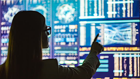  A woman with glasses infront of many screens displaying data