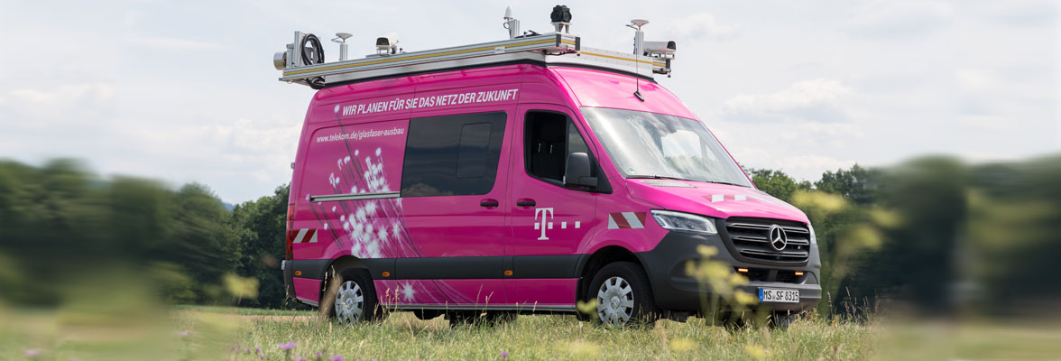 Das T-Surface Car der Telekom fährt auf einer schmalen Straße zwischen Wiesenflächen.