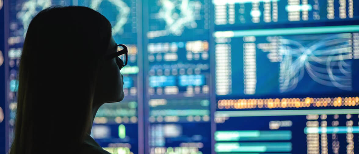 A woman in front of a display wall showing graphs and data.