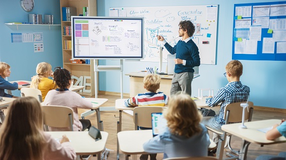 A teacher stands in front of a blackboard and teaches a school class