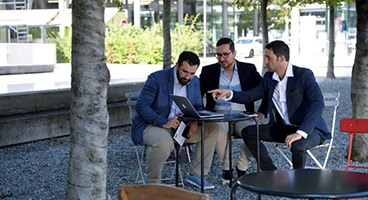 Three young men are working outside on a laptop.