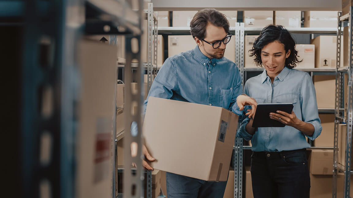 A man and woman standing in a warehouse looking at a tablet