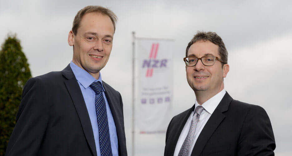 Rolf C. Knemeyer, Managing Partner of NZR, and Robert Holkenbrink, Head of Development and Product Management, in front of an NZR flag.