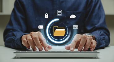 Ein Mann tippt auf einer Tastatur, im Vordergrund des Bildes sieht man digitale Icons wie z.B. eine Cloud Wolke oder Ordner 
