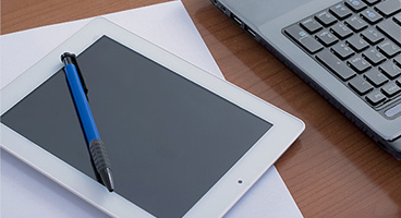 Tablet mit einem Kugelschreiber und Teilansicht einer Laptop Tastatur