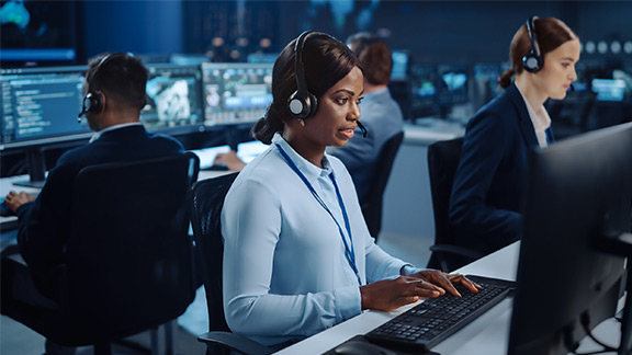 Mehrere Personen mit Headsets sitzen in einem modernen Callcenter an ihren Arbeitsplätzen.