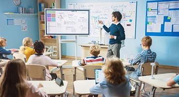 A teacher stands in front of a blackboard and teaches a school class