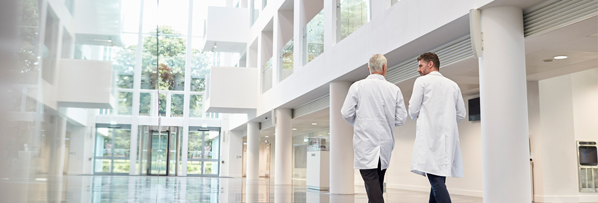 Two gentlemen in white lab coats walk side by side in an entrance hall and talk