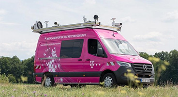 Das T-Surface Car der Telekom fährt auf einer schmalen Straße zwischen Wiesenflächen.