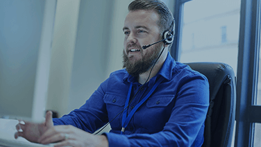 Bärtiger, junger Mann telefoniert mit Headset im Büro.