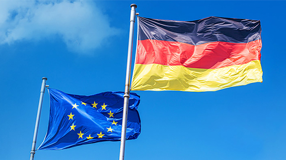 The European and German flags waving in the wind against a blue sky
