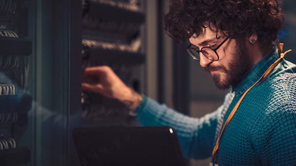 Ein Techniker mit Laptop in der Hand arbeitet am Serverschrank.