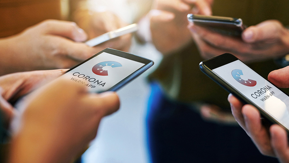 Several hands with mobile phones showing the splash screen of the Corona warning app.