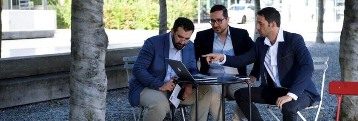 Three young men working on a laptop outdoors.