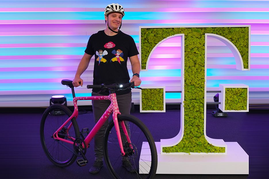 German Santini mit Fahrrad neben einem bepflanztem horizontalen T der Telekom