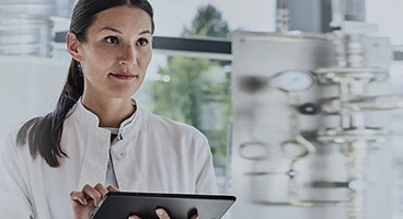 Eine Frau im weißen Kittel in einem Labor mit einem Tablet in der Hand