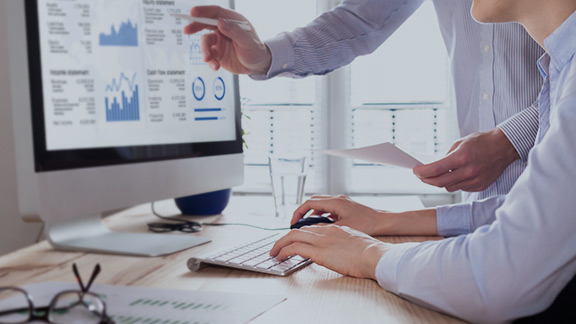 Two individuals sitting at a computer analyzing data.