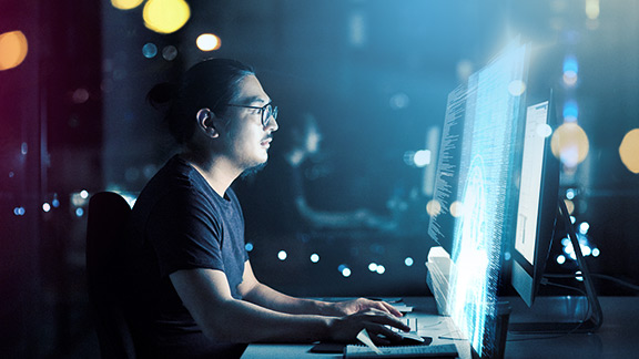 A man sits in front of a large screen in a darkened room 