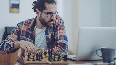 Mann der auf ein Laptop schaut während er auf einem Schachbrett spielt